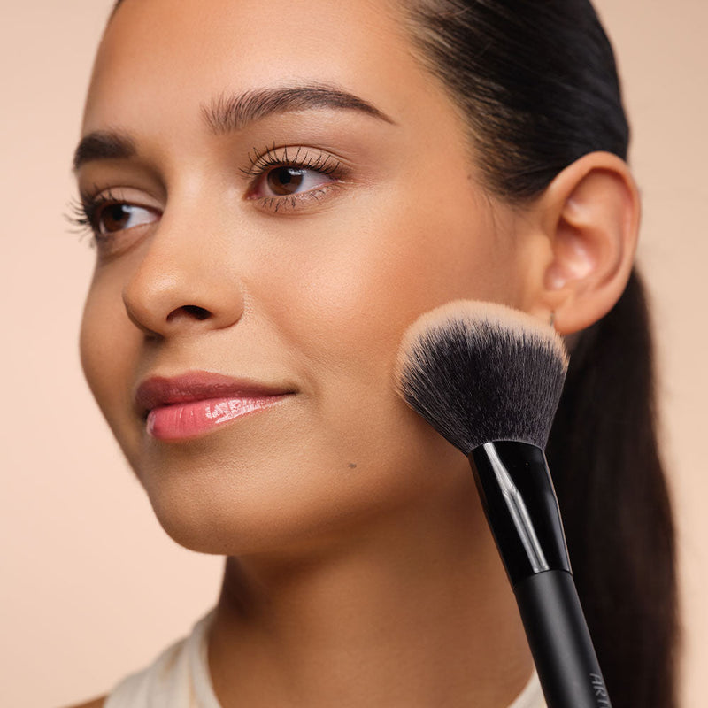 Frau mit bronzed Teint posiert mit einem Bronzer neben ihrem Gesicht