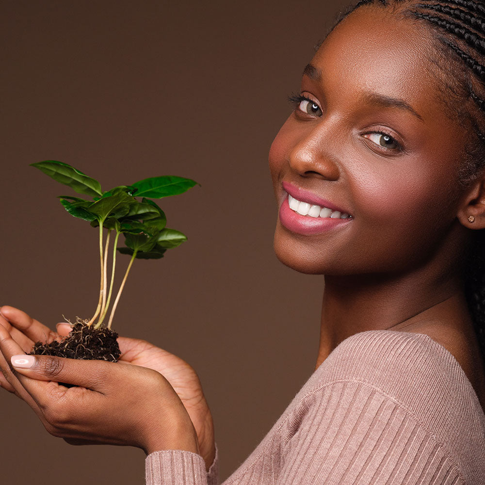 Frau hält einen Pflanzenspross in ihrer Hand und lächelt