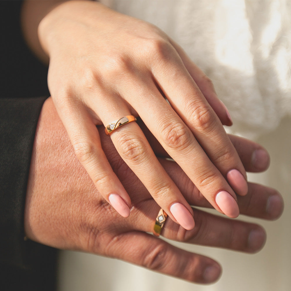 Detailfoto der übereinandergelegten Hände, jeweils mit Ehering, eines Brautpaares. 