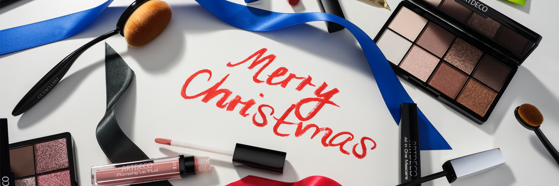 Mood-Bild mit verschiedenen Artdeco Make-up Produkten die das Wort „Merry Christmas“ umgeben