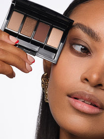 Close-up auf das Gesicht des Models, mit Fokus auf die Augen, an denen ein befüllte Beauty Box mit in dem Look verwendeten Lidschatten gehalten wird