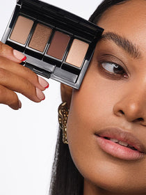 Close-up auf das Gesicht des Models, mit Fokus auf die Augen, an denen ein befüllte Beauty Box mit in dem Look verwendeten Lidschatten gehalten wird