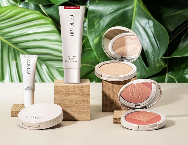 Alle Teint Produkte der Green Couture Porudktlinie werden auf Holzklötzen schön vor einem Hintegrund aus Blättern präsentiert