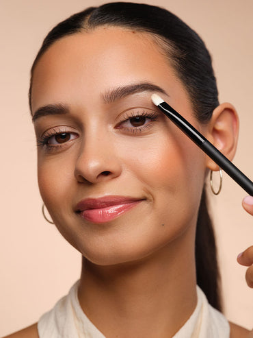 Model hält kleinen Lidschatten-Pinsel unter die Auge, um zu zeigen das dort Highlighter aufgetragen wird