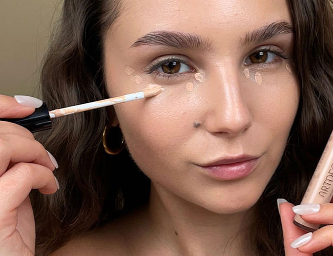 Das Model trägt langanhaltenden Concealer punktuell unter ihren Augen auf, um Unebenheiten und Augenringe zu kaschieren