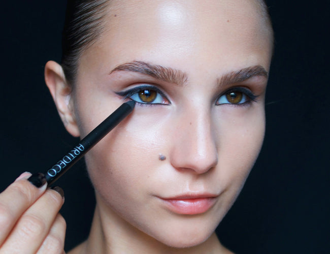 Das Model trägt schwarzen Eyeliner auf, um ihr Augen-Make-up zu intensivieren