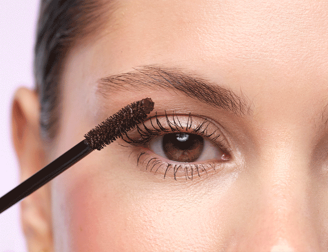 Close-ups auf das Auge des Models, an welchem die braune Mascara sowie ein transparentes Augenbrauen-Gel aufgetragen wird