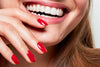 Eine Hand mit rotlackierten Nägeln wird vor einen lachenden Mund gehalten