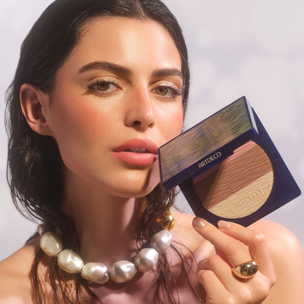 Anwendung des All Seasons Bronzing Powder mit halbgeöffneten Produkt um die Textur und Farbe  zu sehen