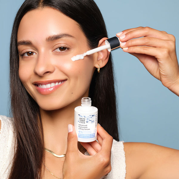 Brünettes Model trägt das Advanaced Hyaluronic Lifting Serum mit einer Pipette auf ihre Wange auf. Das Produkt befindet sich in einem hochwertigen Glasflakon.