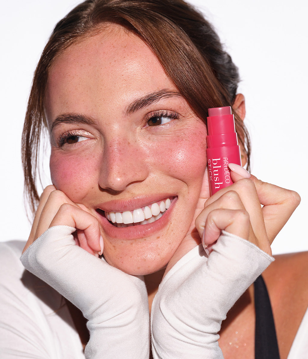 Rothaariges Model hält den Blush Stick in der Hand und lacht freundlich und ausgelassen in die Kamera