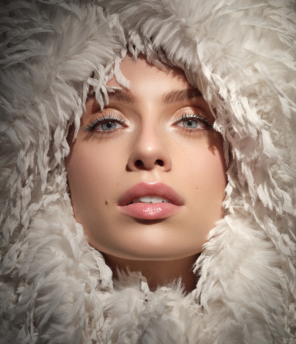 Fokus auf das mit den Metallic Eye Liner geschminkte Gesicht des Models, welches von federähnlichem Stoff von den Ärmeln ihrer Jacke umgeben ist.