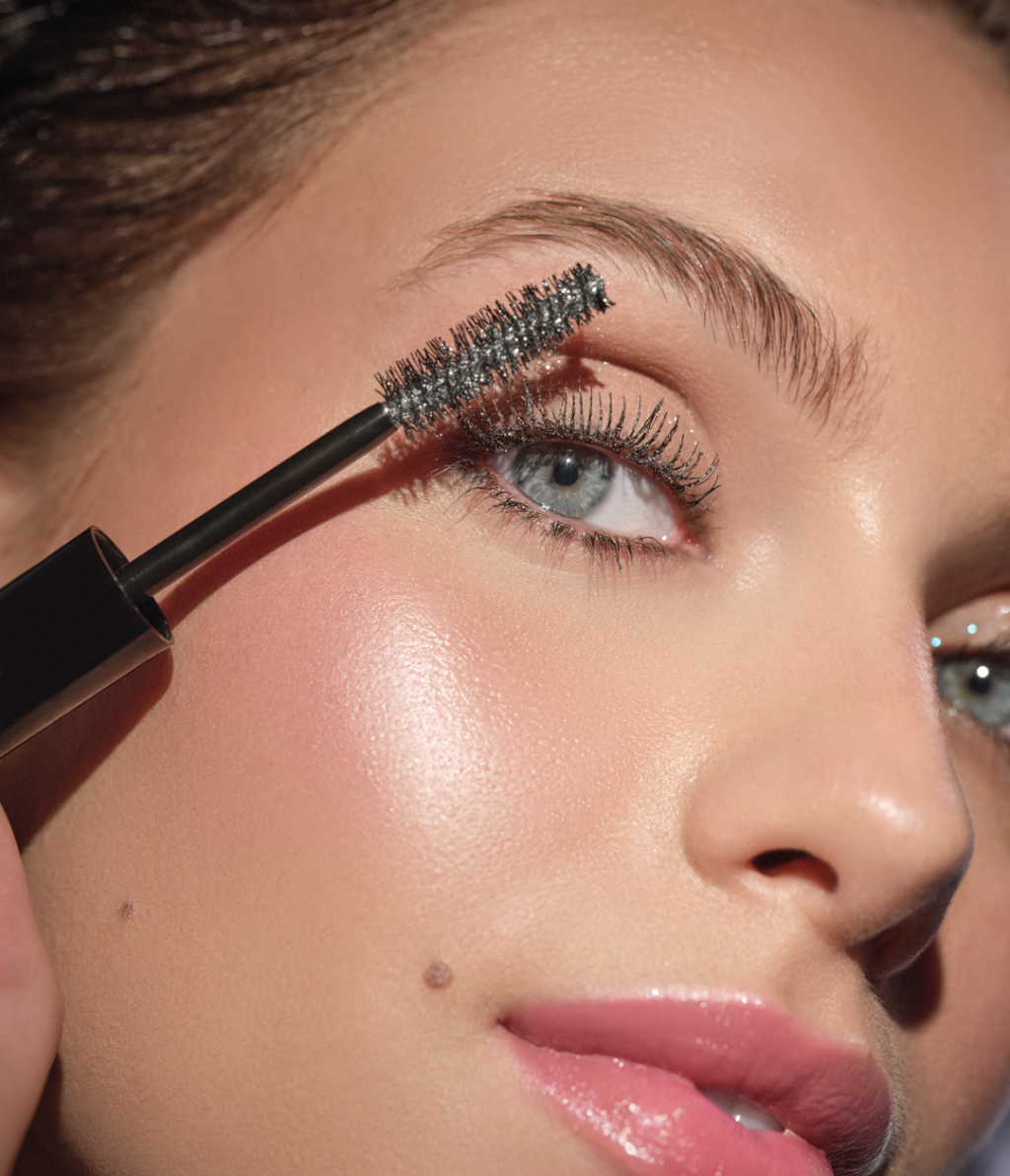 Close-up auf das Auge des Models, auf welches die Eyelights Mascara aufgetragen wird, und die Wimpern mit einem silbernen Glitzer-Schleier überzogen werden.