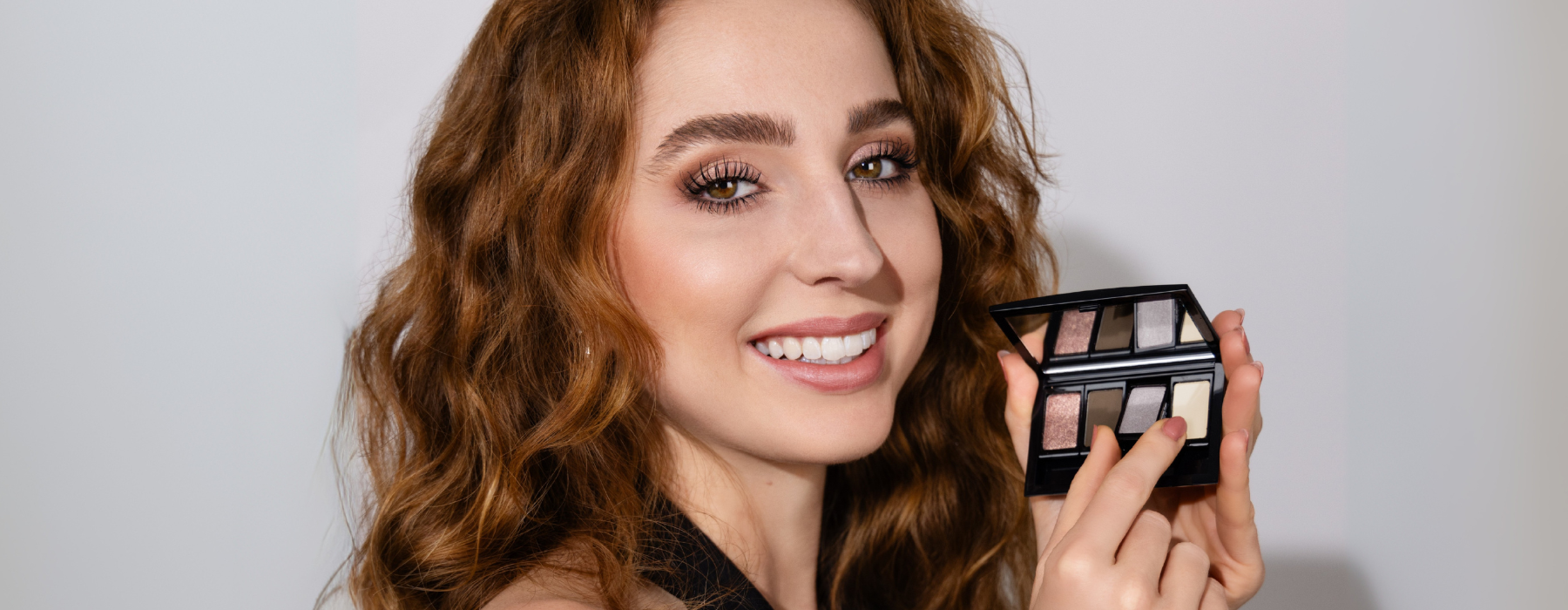 Model mit rötlichen Haaren hält eine Beauty Box Quattro mit ausgewählten Lidschatten in der Hand und lächelt dabei um die Jubiläums-Kollektion von ARTDECO zu feiern