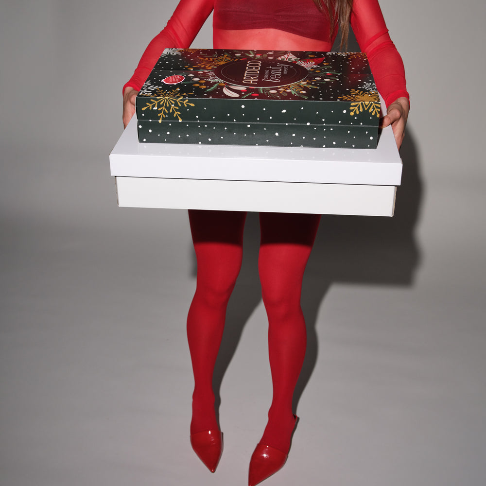 Eine Person in rotem Outfit und roten Schuhen hält zwei große Geschenkboxen vor sich. Die obere, dunkelgrüne Box ist die ARTDECO Adventskalender, darunter befindet sich eine größere weiße Box.