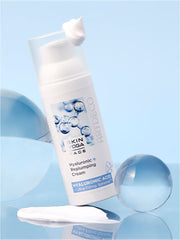 Die Hyaluronic + Replumping Cream vor einem hellblauen Hintegrund umgeben von verschieden großen Glaskugeln. Auf dem Deckel ist etwas Creme-Klecks zu sehen.