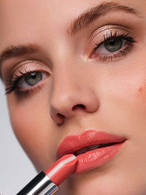 Close-up auf das Gesicht des Models, mit Fokus auf die Lippen, an denen ein aprikotfarbener Lippenstift gehalten wird