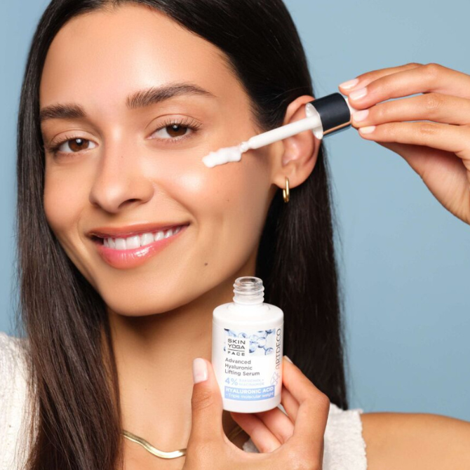 Brünettes Model trägt das Advanaced Hyaluronic Lifting Serum mit einer Pipette auf ihre Wange auf. Das Produkt befindet sich in einem hochwertigen Glasflakon.