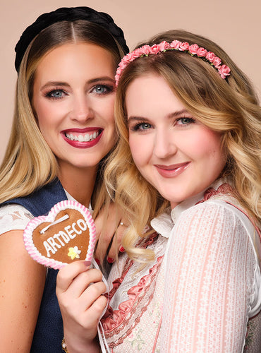 Beide Models mit fertigem Oktoberfest Make-up lachen in die Kamera, es wird ein Lebkuchenherz in der Hand gehalten