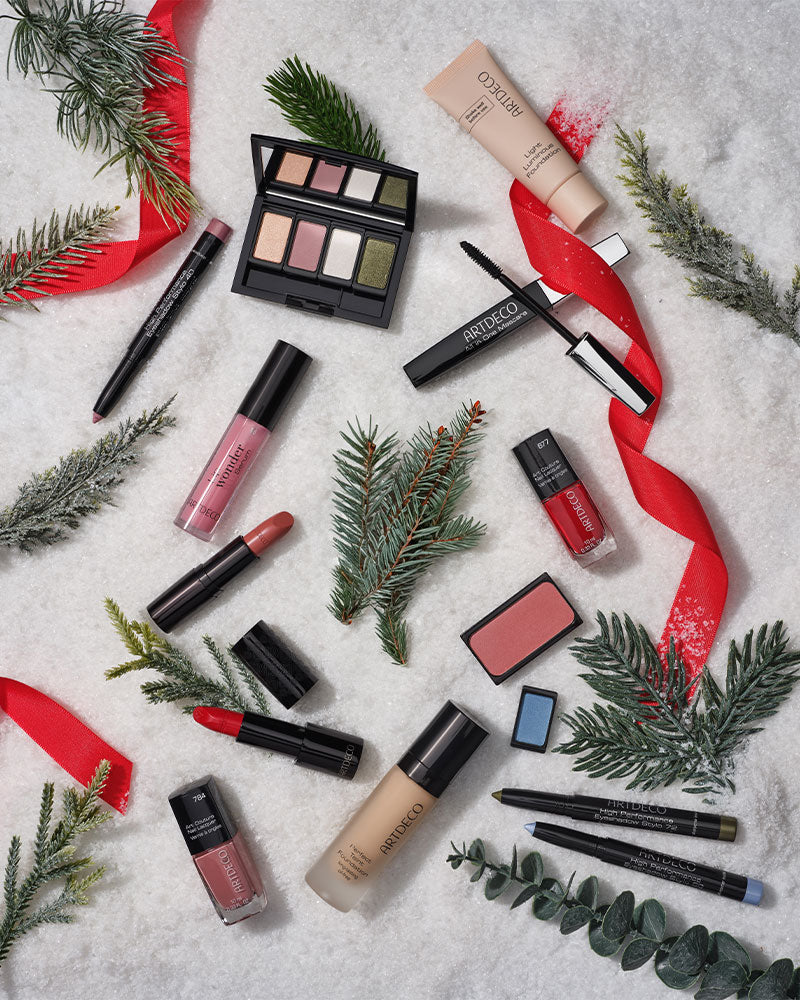 Unterschiedliche Kosmetik Produkte von ARTDECO liegen auf einem Untergrund aus Schnee und sind umgeben von einzelnen Tannenzweigen