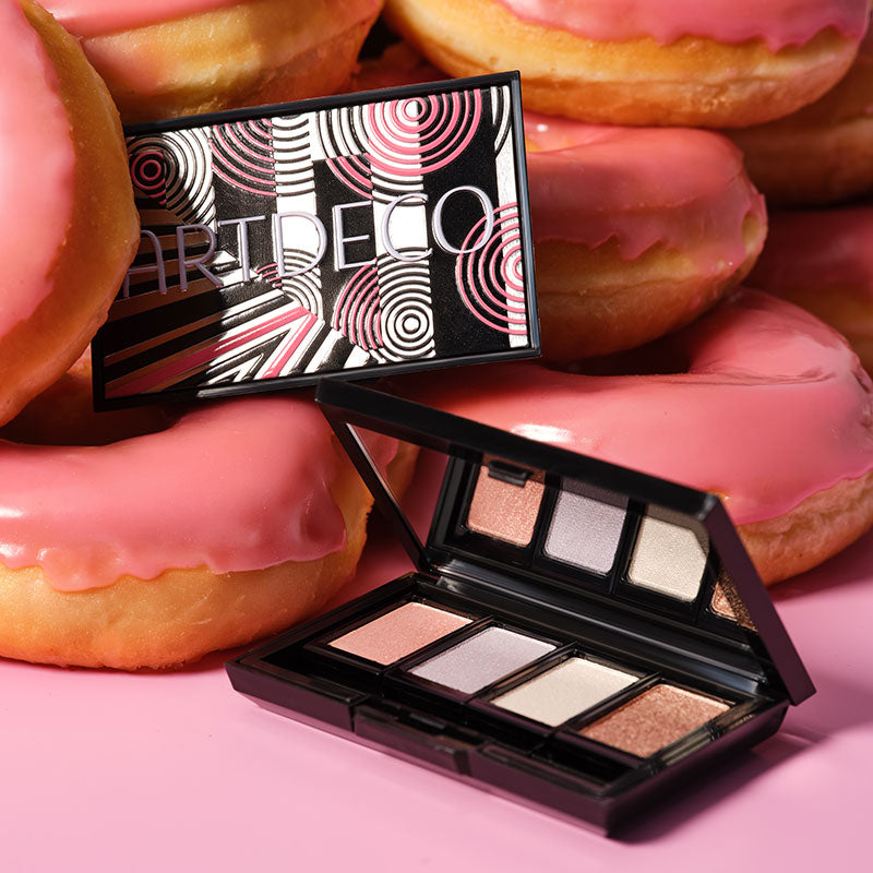 Beauty Box Quattro im limitierten 40 Jahre ARTDECO Design in Rosa und dazugehörigen Lidschatten, liegt auf einem rosa Untergrund und ist umgeben von rosa Donuts