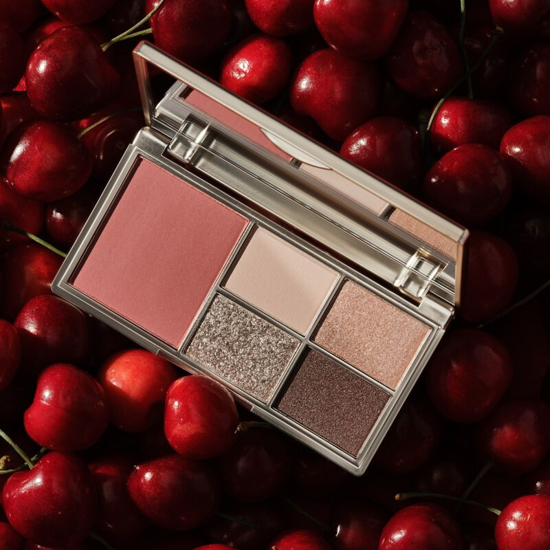 Geöffnette Illusion Palette for Cheeks & Eyes liegt auif einem Untergrund auf Kirschen