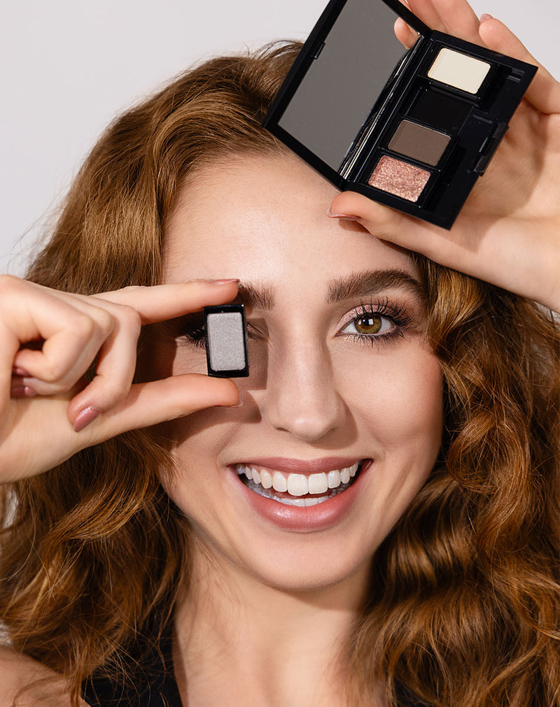 Model mit rötlichen Haaren hält eine Beauty Box Quattro mit ausgewählten Lidschatten in der Hand und lächelt dabei um die Jubiläums-Kollektion von ARTDECO zu feiern