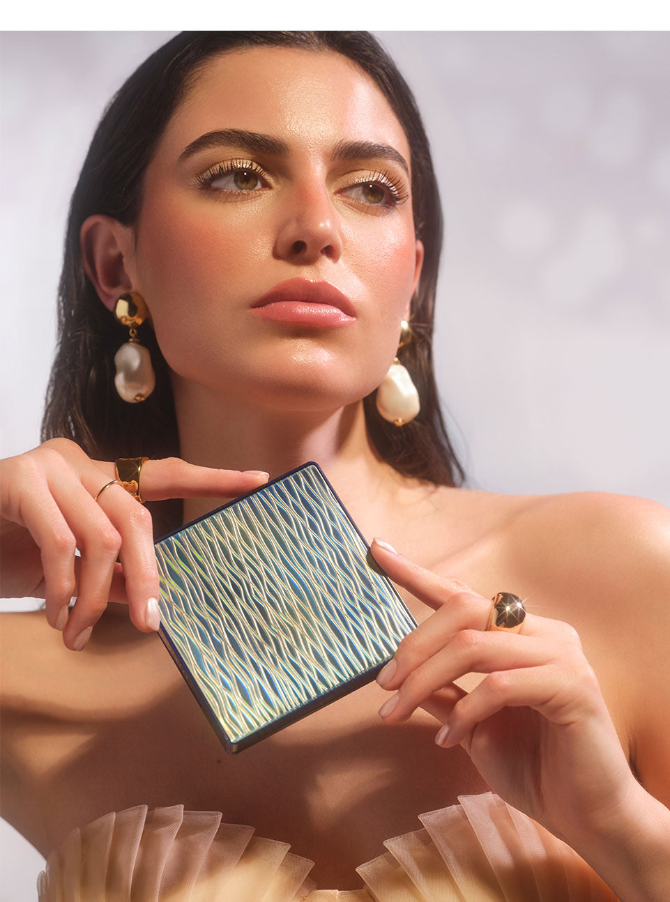 Brünettes Model mit einem sommerlichen und glowy Make-up, haält das All Seasons Bronzing Powder in den Händen, sodass man die wellenartige Verpackung gut erkennen kann