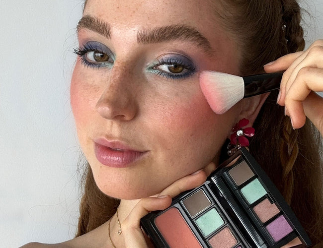 Rosiger Blush wird mit Blusher Brush aufgetragen während Frau die Beauty Box Quadrat in der Hand
