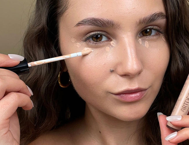 Das Model trägt langanhaltenden Concealer punktuell unter ihren Augen auf, um Unebenheiten und Augenringe zu kaschieren 