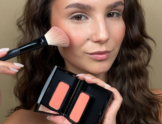 Apricotfarbener Blush wir mit einem abgeschrägten Pinsel seitlich auch auf die Wange des Models aufgetragen für ein frisches Sommer Make-up