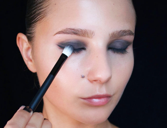 Das Model trägt schwarzen Lidschatten mit einem Pinsel auf, um dem Augen-Make-up einen verruchten Look zu verleihen. 