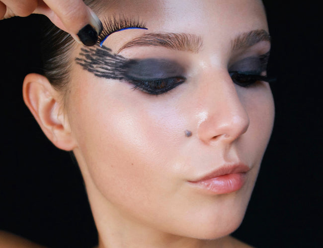 Model zeigt, wie die künstlichen Wimpern für das einfache Halloween-Make-up richtig angebracht werden.