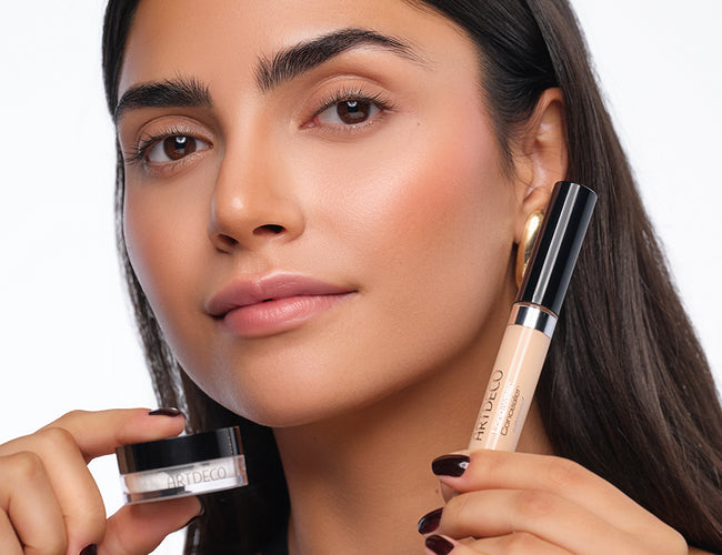 Das Model hält den ARTDECO Longwear Concealer und das Eye Brightening Setting Powder, mit dem der Concealer fixiert wurde, neben das Gesicht.