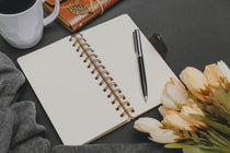 Ein Notizbuch mit Ring-Bindung einem Kugelschreiber und einem Strauß Blumen sind zu sehen