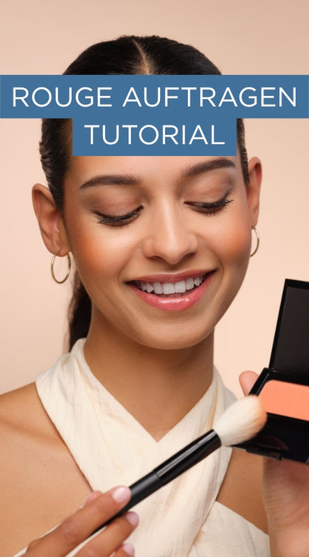 Model lächelt und nimmt mit einem Pinsel orangefarbenes Rouge auf. Schriftzug „Rouge auftragen Tutorial“ kündigt das verlinkte Make-up-Tutorial an.