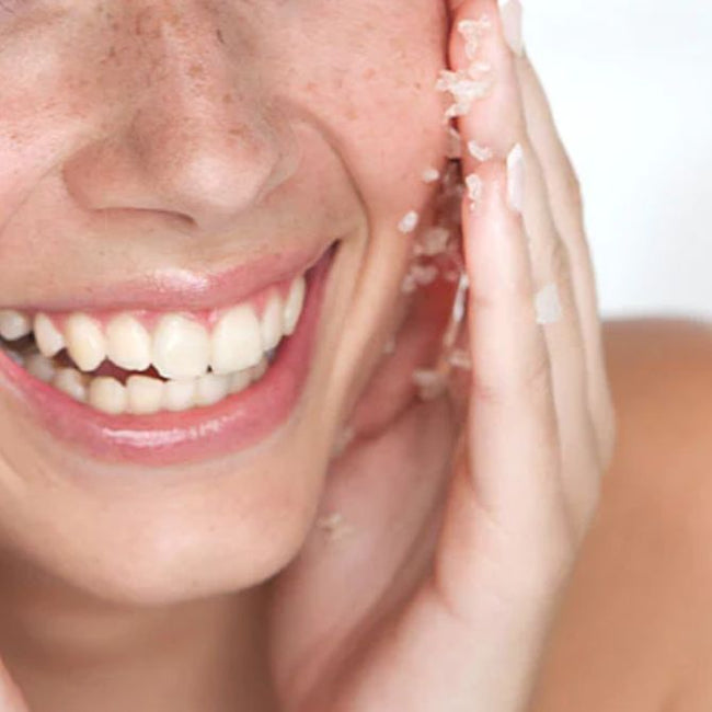 Lächelndes Model mit Sommersprossen trägt Peeling auf ihr Gesicht auf.