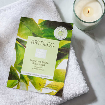 Hyaluronic Hydra Sheet Mask liegt auf einem Handtuch neben einer Kerze.