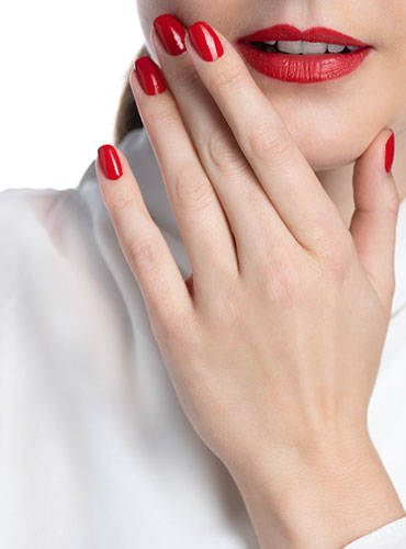 Model mit roten Lippen hält Hand mit frische Maniküre und roten Nagellack an die Wange zum posieren