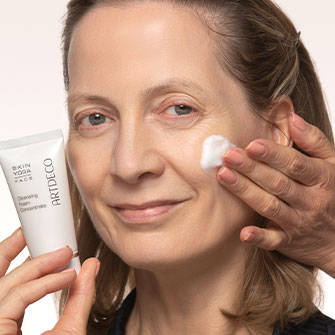 Frau hält eine Tube mit Gesichtspflege in der Hand und trägt sich das Produkt auf die Wange auf