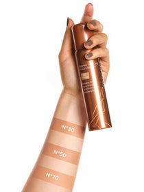Alle Farben der Spray on Leg Foundation sind auf einem Unterarm aufgetragen und ein Produkt wird in der Hand gehalten. 