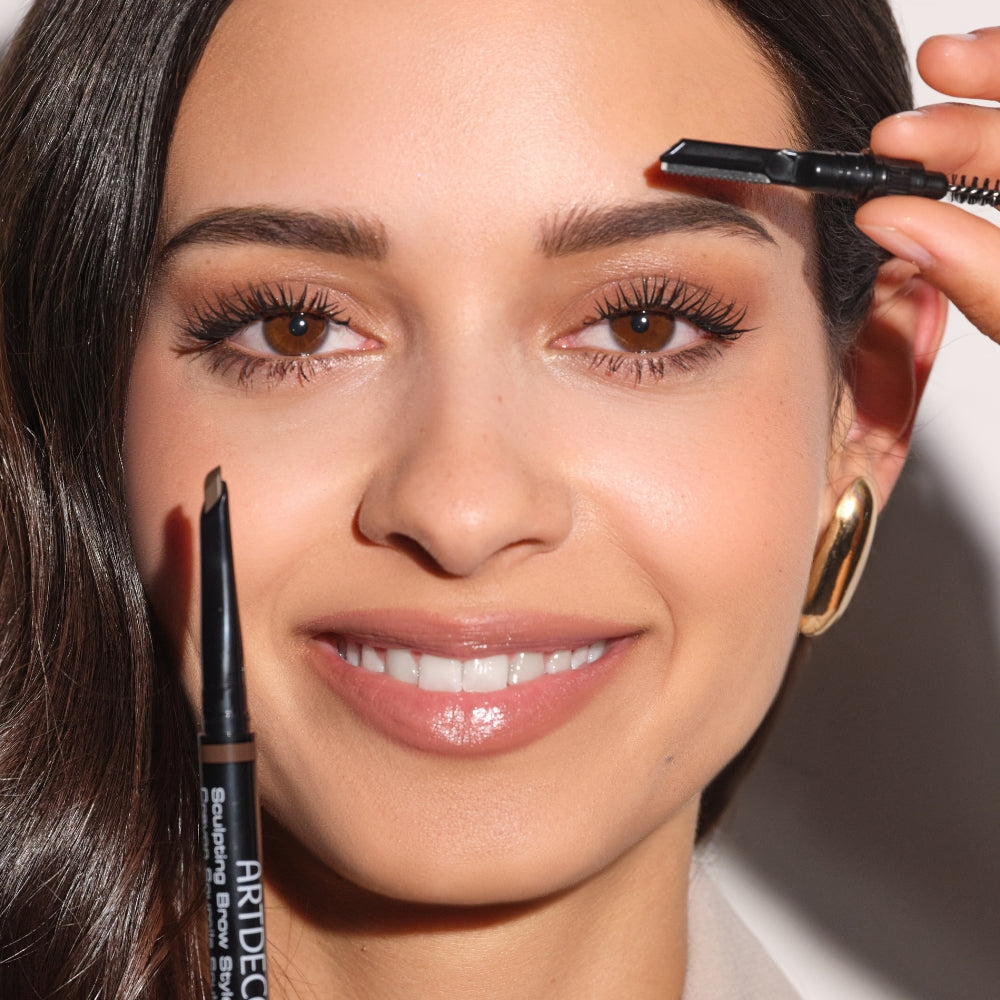 Model hält den ARTDECO Sculpting Brow Styler ans Gesicht und zeigt die verschiedenen Enden des Stiftes: Mine, Bürste und Augenbrauenrasierer.