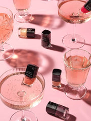 Mehrere Mini Nagellacke in Martini- und Sektgläsern auf rosa Hintergrund 