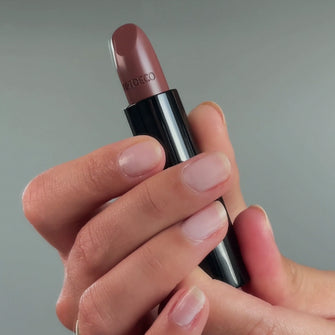 Hände halten den Perfect Color Lipstick in Nuance N°842 - dark cinnamon.