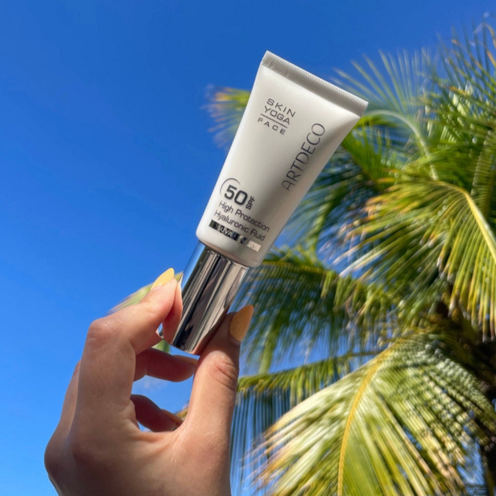 Artdecos High Protection Hyaluronic Fluid SPF 50 mit blauem Himmel und Palmen im Hintergrund.