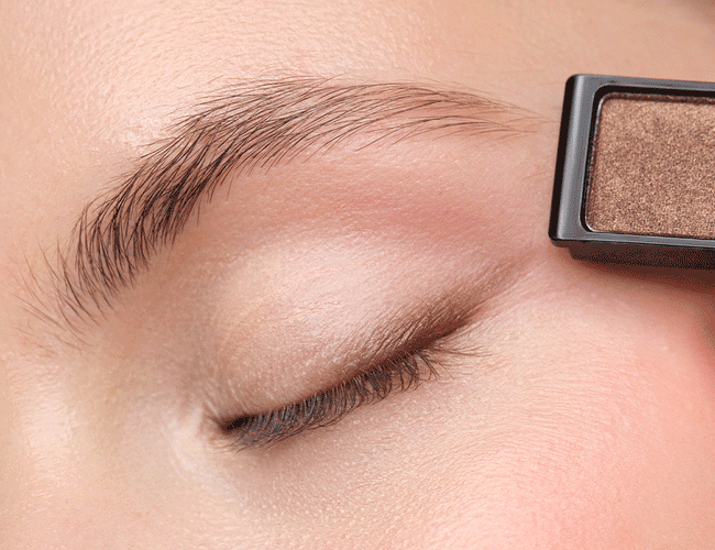 Close-ups auf das Auge des Models, an welchem die Lidschatten für das leichte Tages-Make-up aufgetragen werden, um die Augen gekonnt zu betonen und hervorzuheben