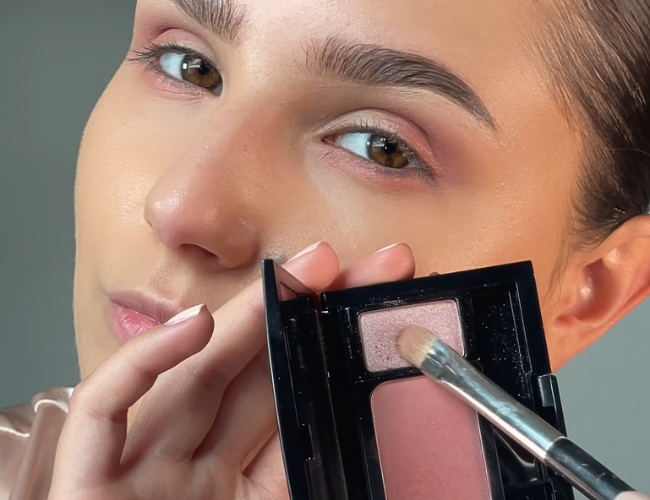 Model trägt einen hellrosanen Lidschatten auf einen flachen Lidschattenpinsel auf.