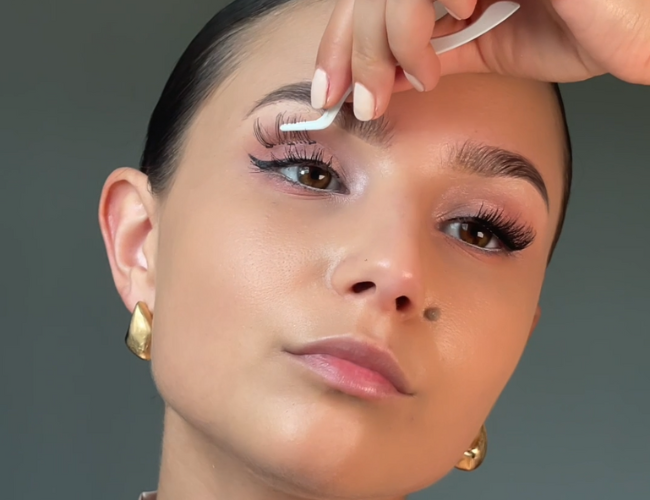 Model trägt sich die künstlichen Wimpern mit einem Applikator auf.