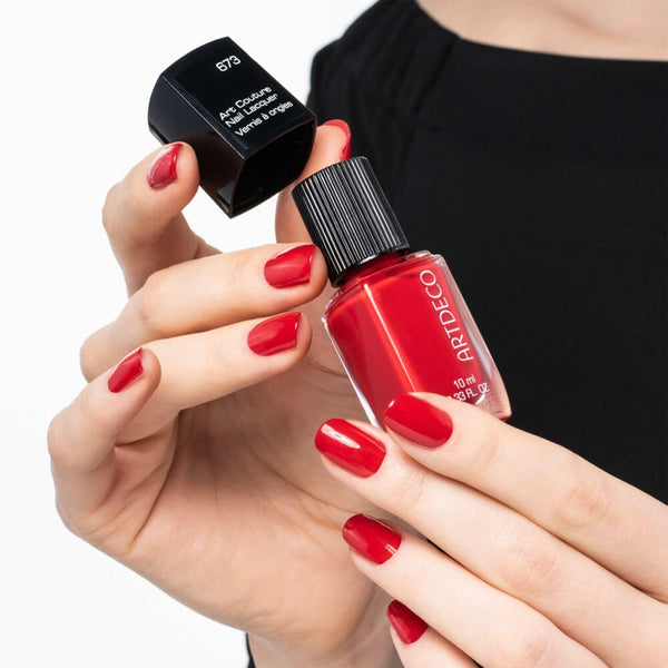 Hand mit rot lackierten Nägeln hält den Art Couture Nail Lacquer in N°673.