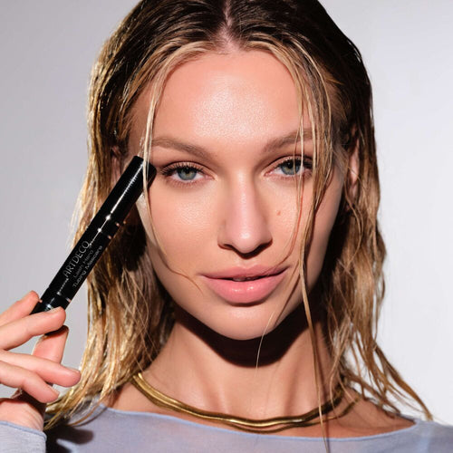 Model mit wet-look Haaren hält ein schwarzes ARTDECO Augen-Make-up-Produkt neben ihr Gesicht und präsentiert einen natürlichen, glänzenden Beauty-Look.